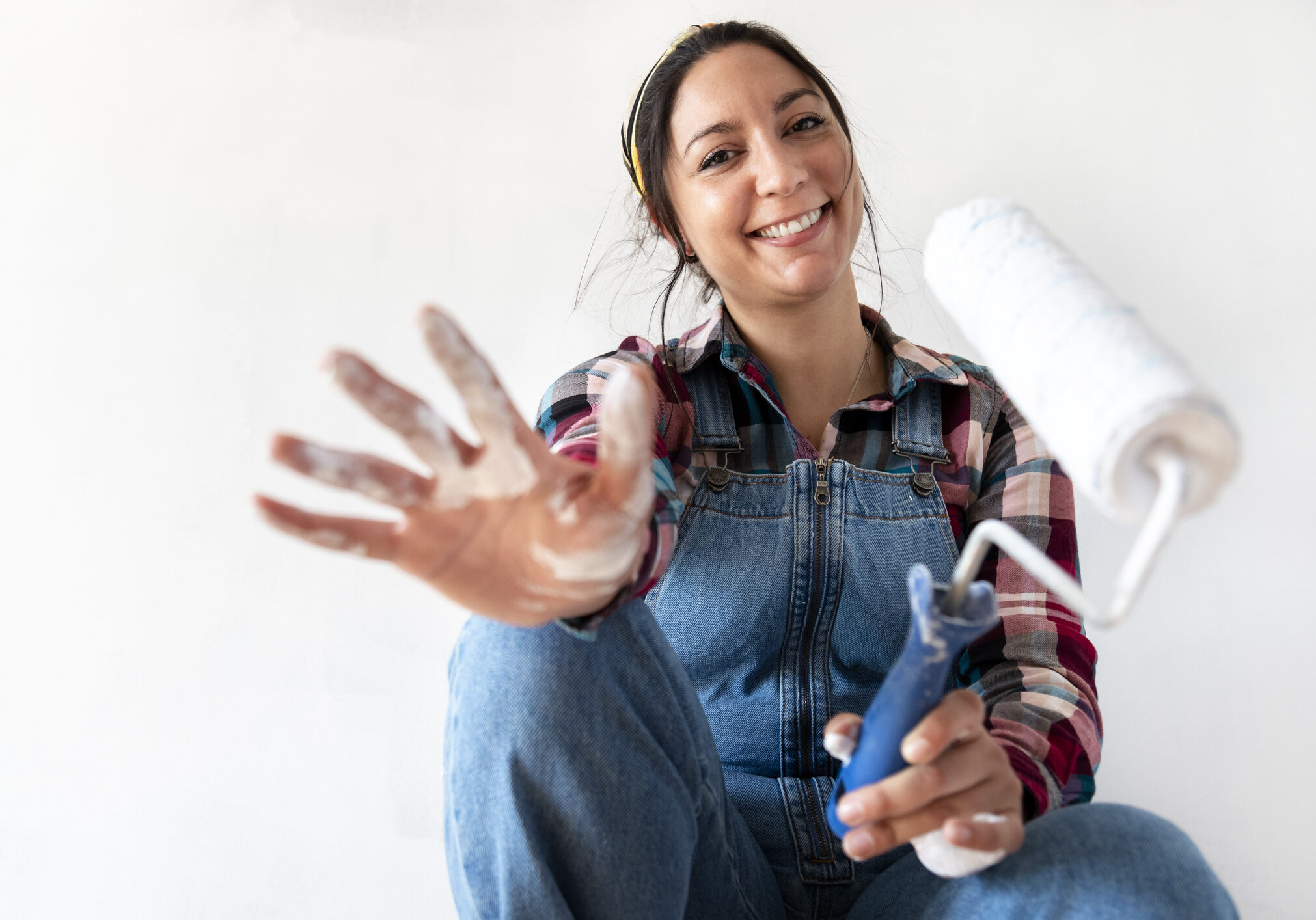 Young brunette woman showing hand with paint looking at camera. Holding a paint roller. Selective focus on woman's face. Renovating concept. Real estate concept. Copy space.